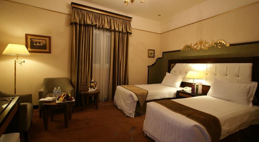 Twin room with wooden furniture and curtains at Manazel Al Ain Mercure Hotel